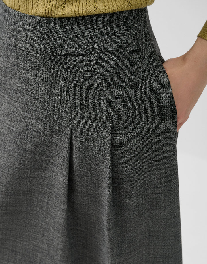 Close-up of a person wearing a gray pleated skirt with a blurred background