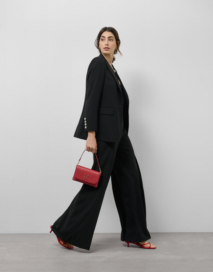 Woman in a black suit holding a red handbag against a plain background