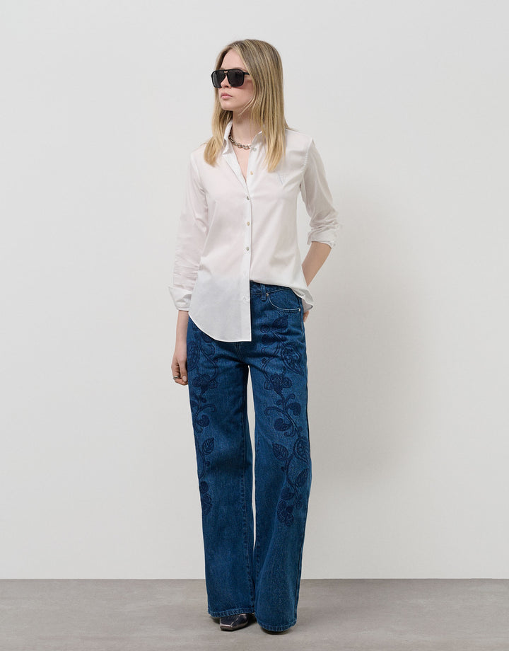 Woman wearing a white shirt and blue jeans against a plain background