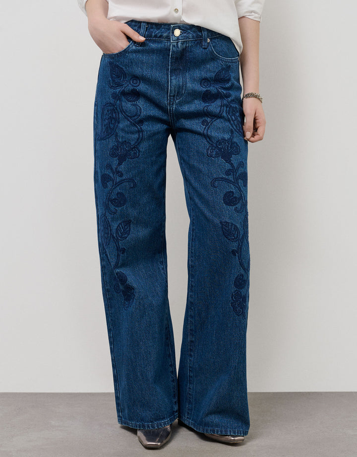 Person wearing blue jeans with floral embroidery on a plain background