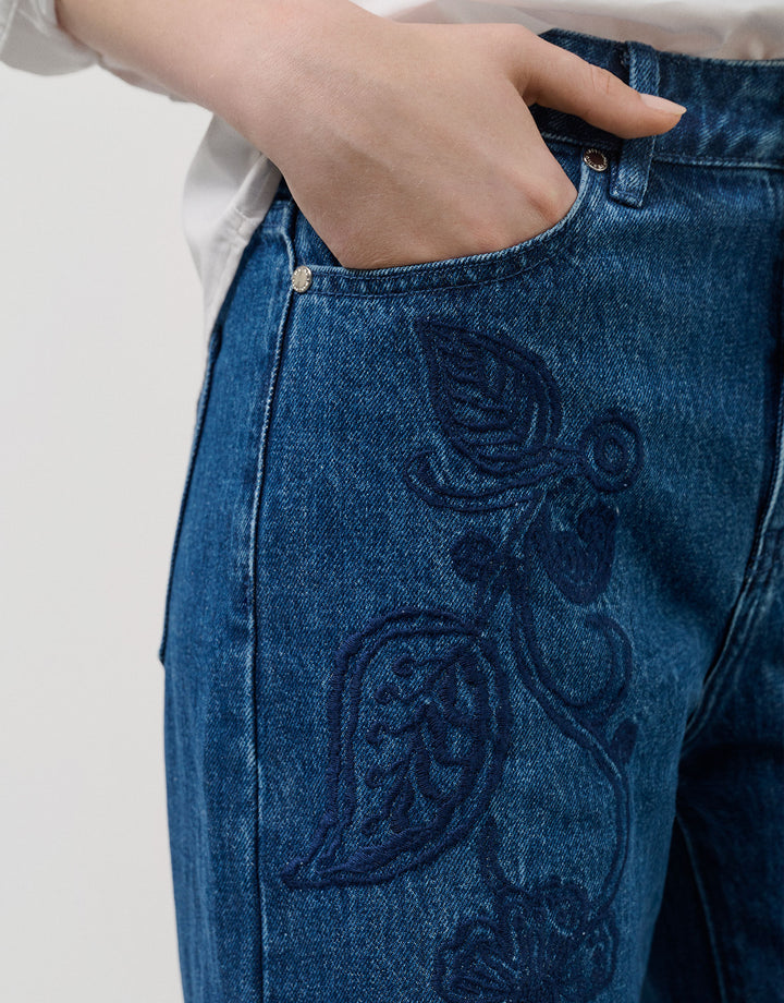 Blue jeans with intricate black embroidery on a plain background