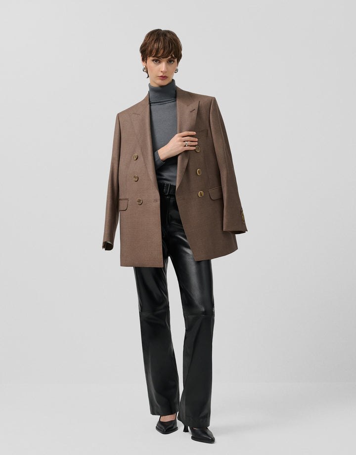 Woman wearing a brown coat, gray turtleneck, and black pants on a light gray background