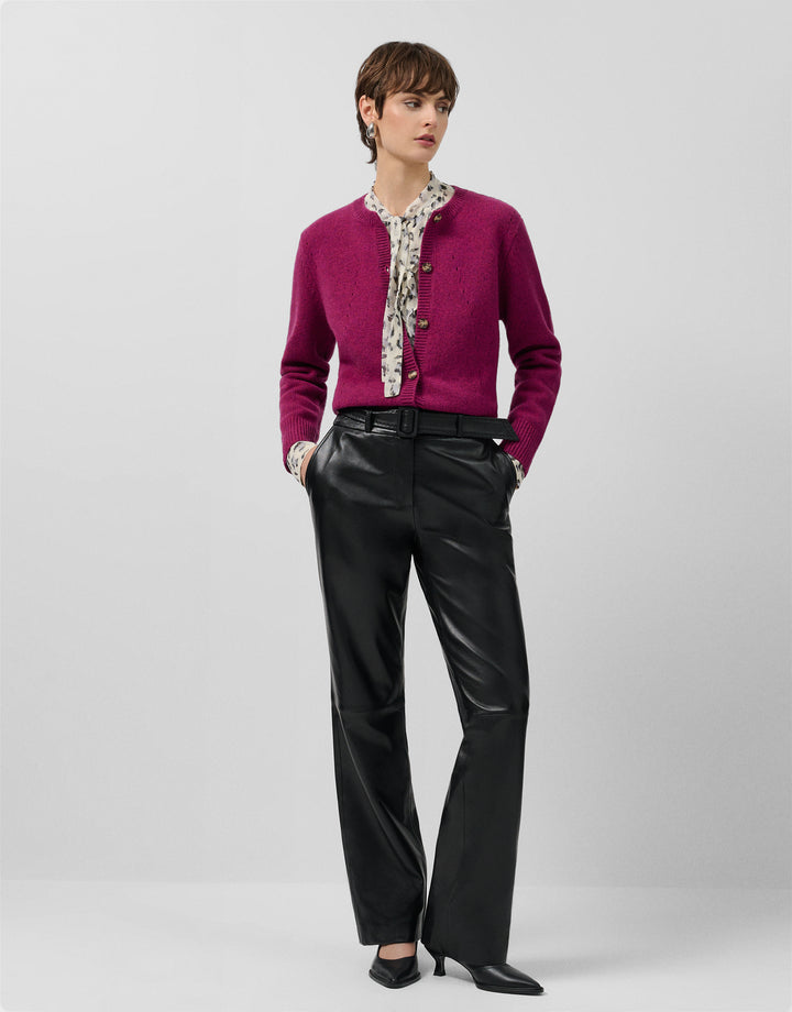 Person wearing a magenta cardigan, black pants, and a patterned scarf on a white background