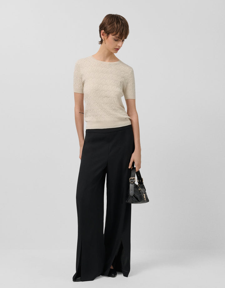 Woman wearing a beige top and black wide-leg pants on a white background