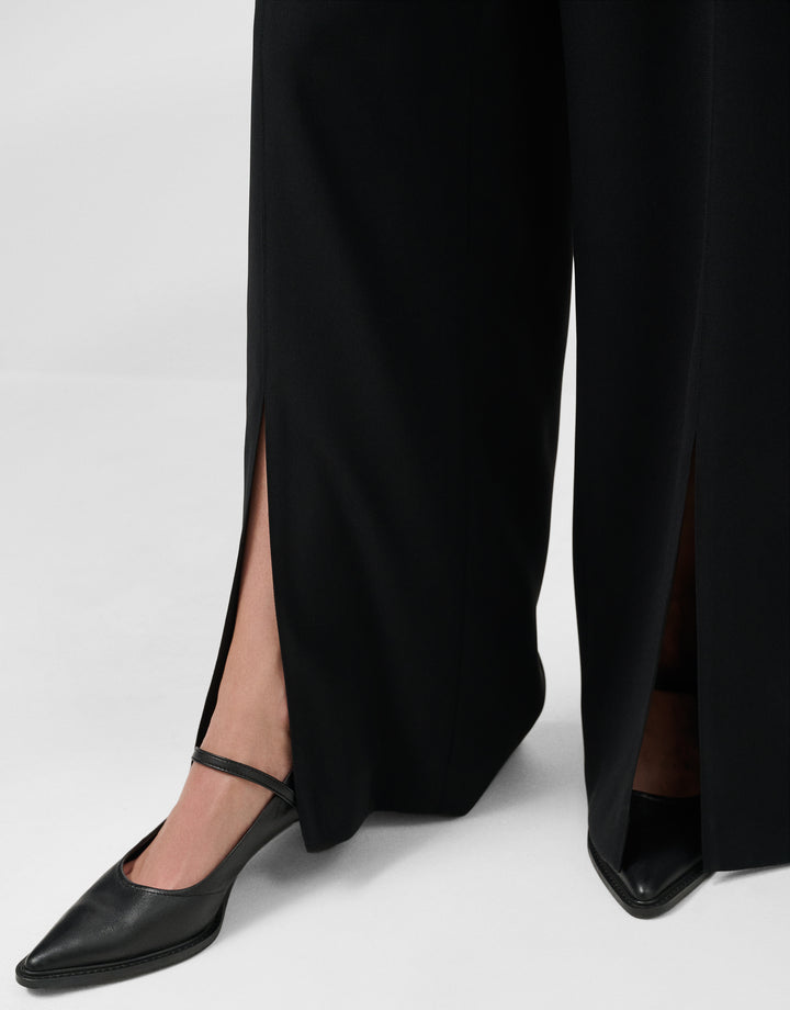 Black pants with a slit and black shoes on a white background