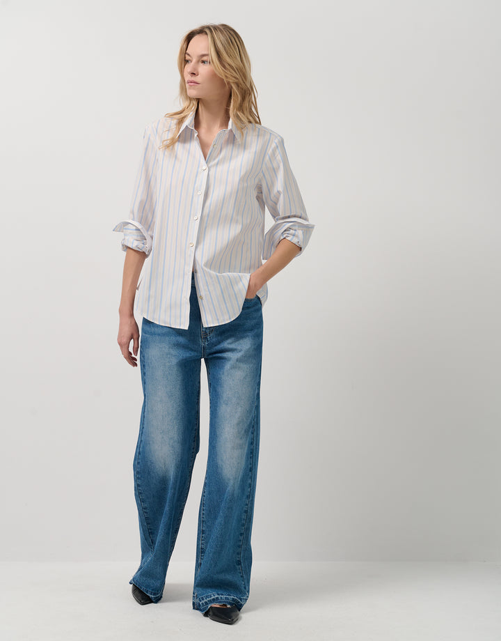 Woman wearing a white striped shirt and blue jeans on a plain background