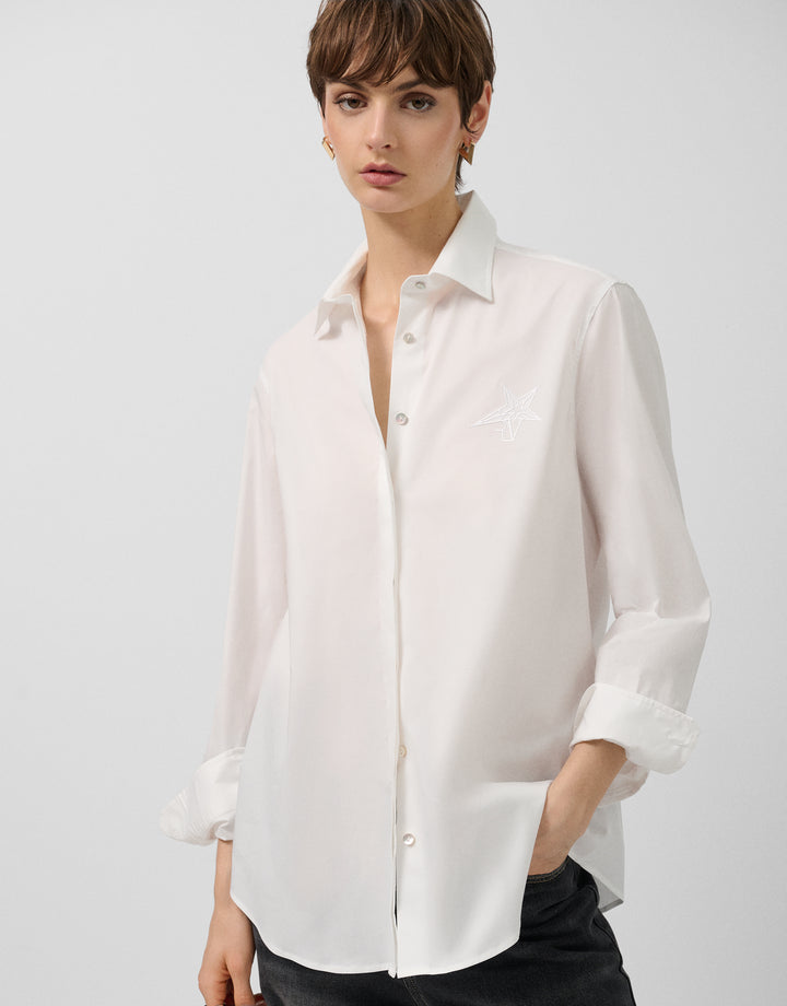 Woman wearing a white shirt with rolled-up sleeves against a plain background