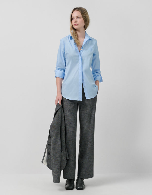 Woman wearing a light blue shirt and gray pants with a gray coat over her shoulder on a white background