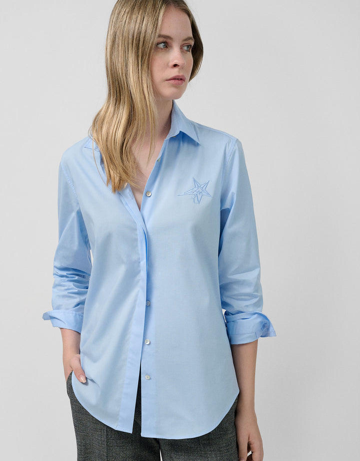 Woman wearing a light blue shirt with a small design on a plain background