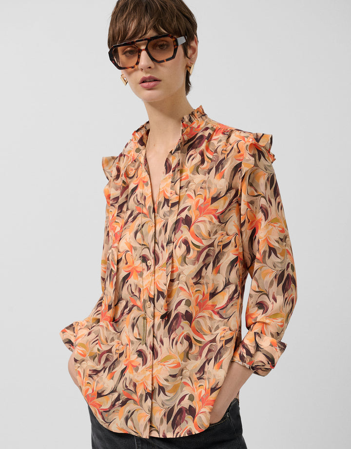 Woman wearing a patterned shirt with rolled-up sleeves on a light gray background