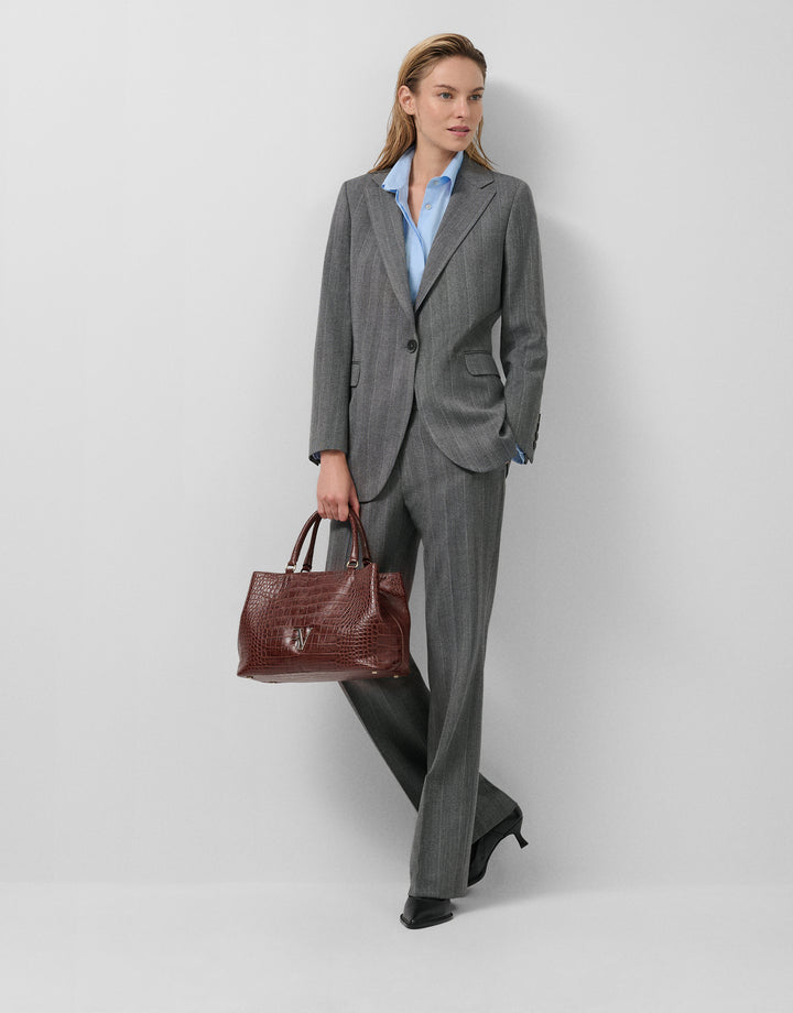 Woman in a gray suit holding a brown handbag on a white background
