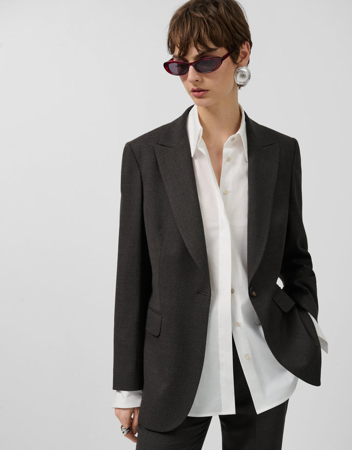 Person wearing a black blazer over a white shirt on a plain background