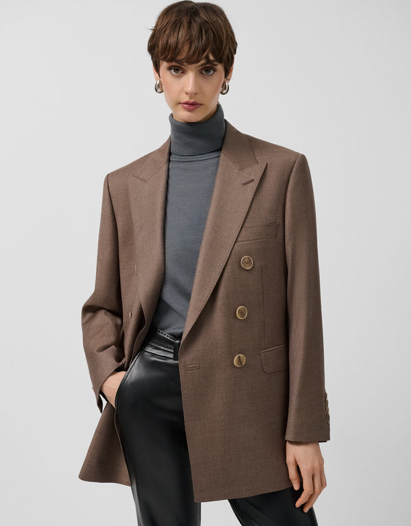 Woman wearing a brown blazer over a gray turtleneck and black pants on a light gray background