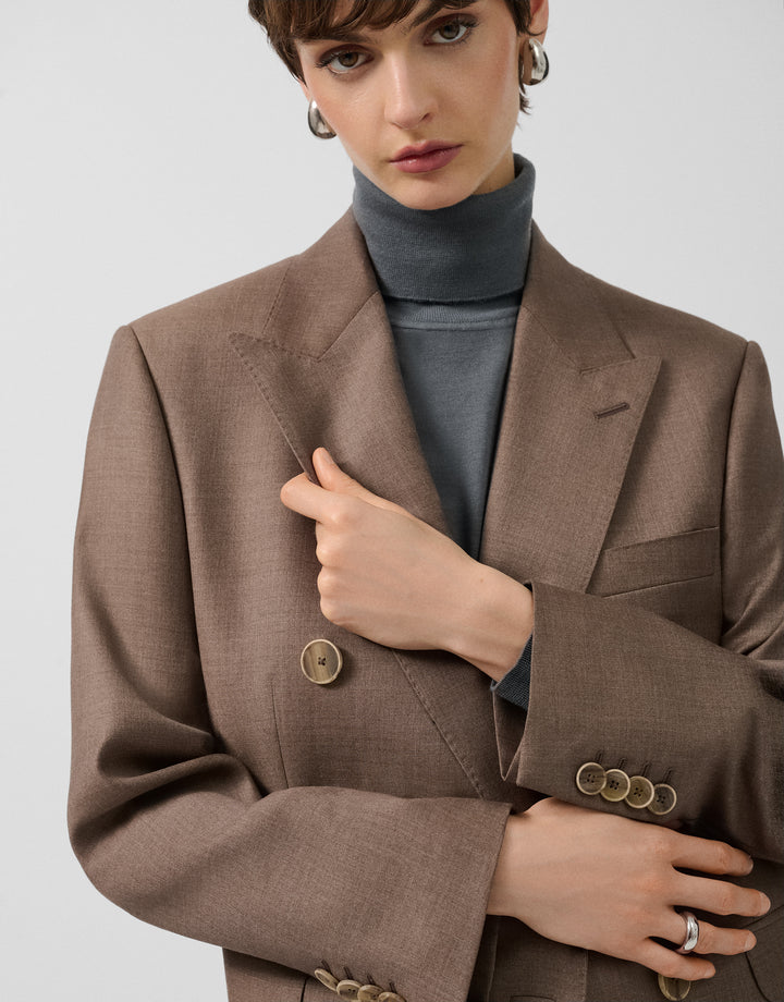 Woman wearing a brown blazer with gold buttons on a plain background