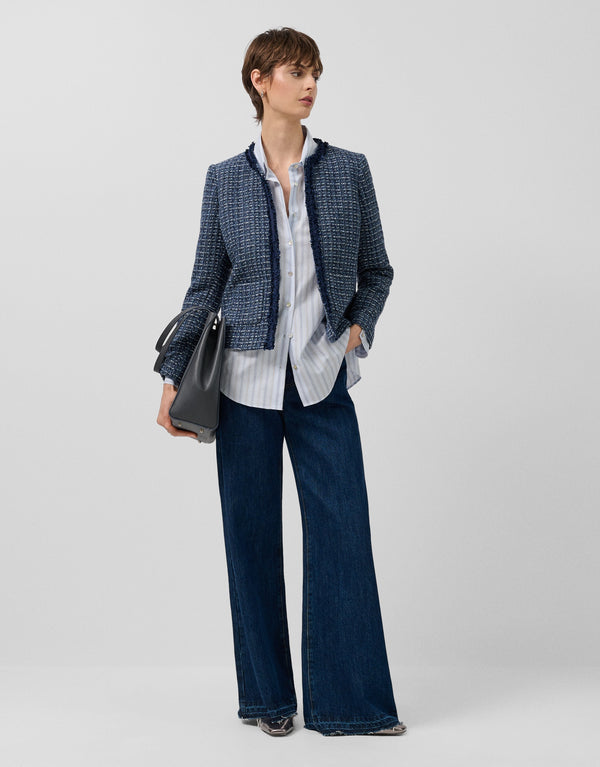 Woman wearing a blue checkered blazer, white shirt, and dark jeans on a light gray background