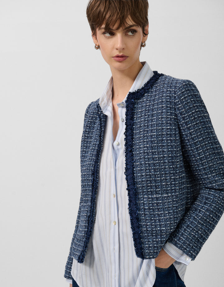 Woman wearing a blue textured jacket over a white shirt on a light gray background