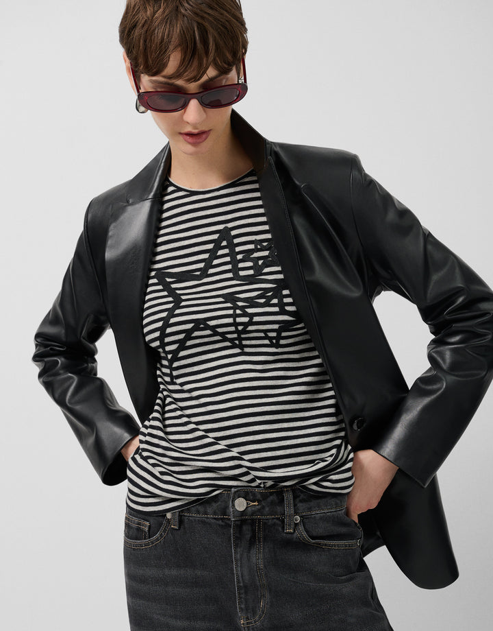 Person wearing a black leather jacket, striped shirt, and sunglasses on a plain background