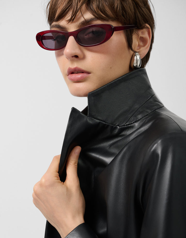 Person wearing a black leather outfit with red sunglasses on a plain background
