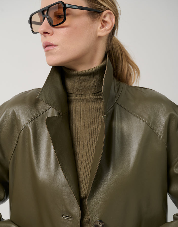 Person wearing a green jacket and sunglasses against a neutral background