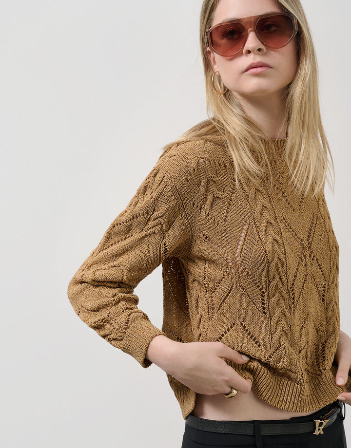 Woman wearing a brown cable knit sweater and sunglasses on a plain background