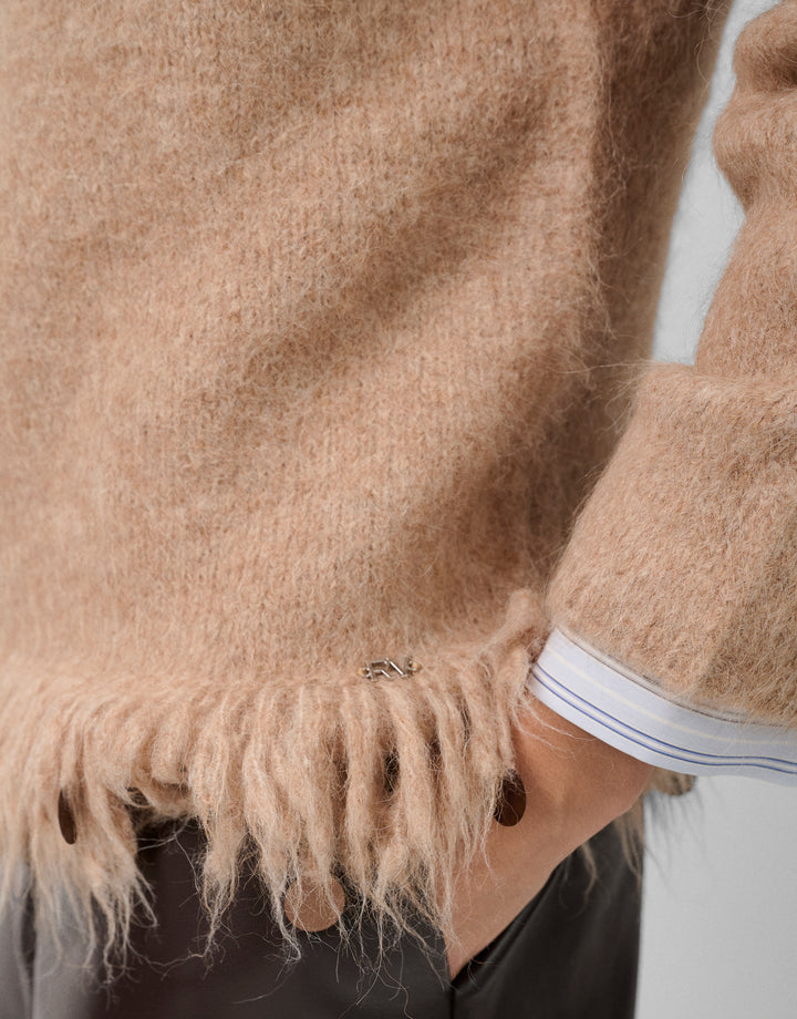 Close-up of a person wearing a beige sweater with frayed edges.