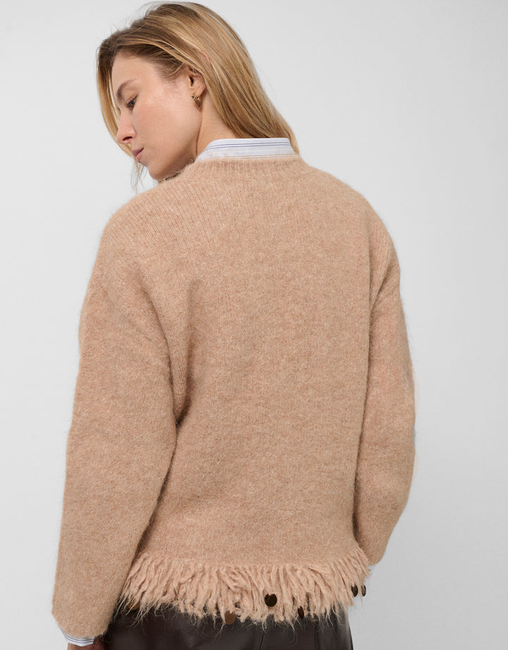 Woman wearing a beige sweater with fringe details on a white background