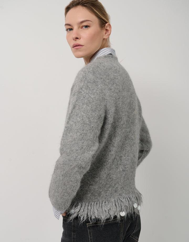 Person wearing a gray sweater with fringe details on a plain background