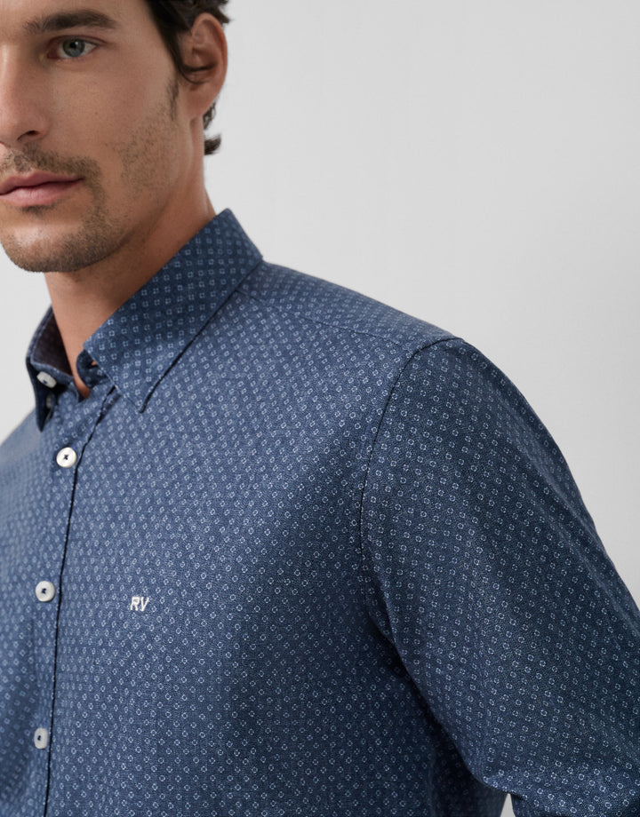 Man wearing a blue patterned shirt with a visible brand logo on a gray background