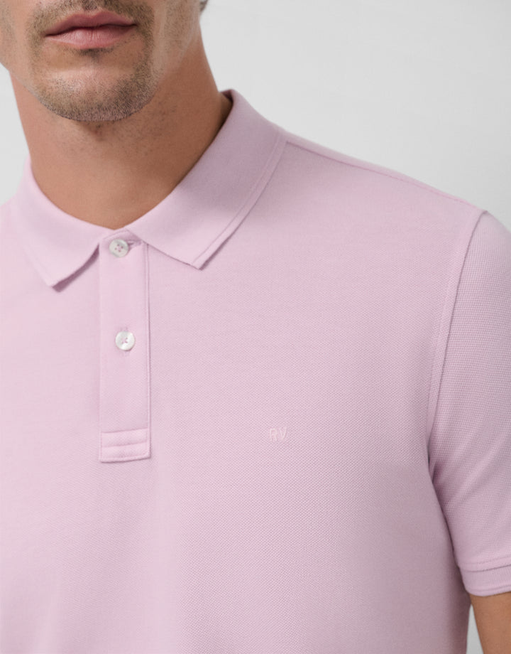 Close-up of a person wearing a light pink polo shirt against a white background