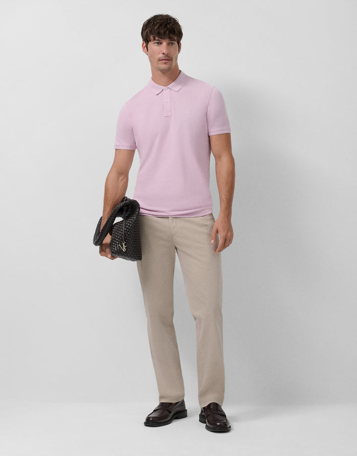 Man wearing a light pink polo shirt and beige pants holding a black textured bag on a white background