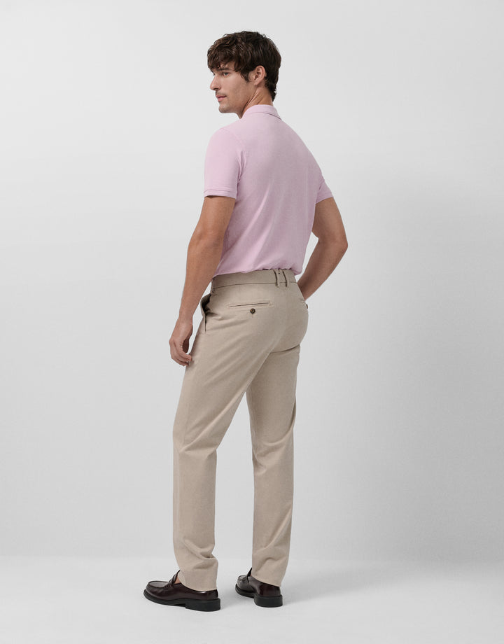 Man wearing a light pink polo shirt and beige pants on a white background