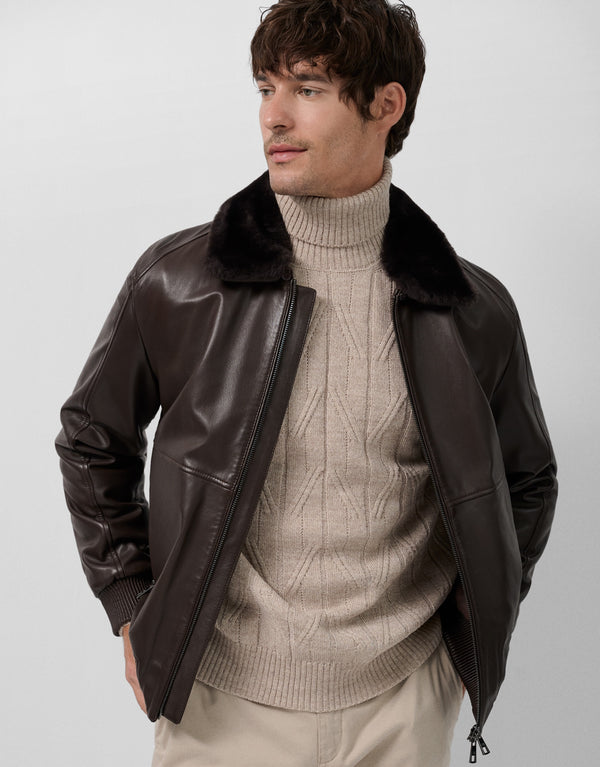 Man wearing a brown leather jacket with fur collar over a beige turtleneck sweater on a white background
