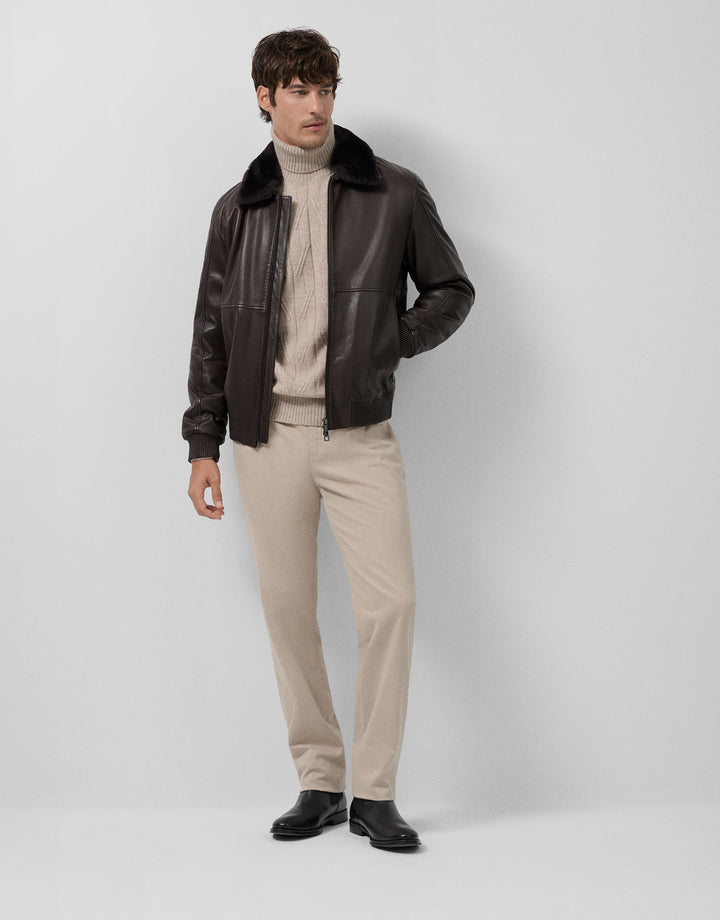 Man wearing a black leather jacket over a beige sweater and pants on a white background