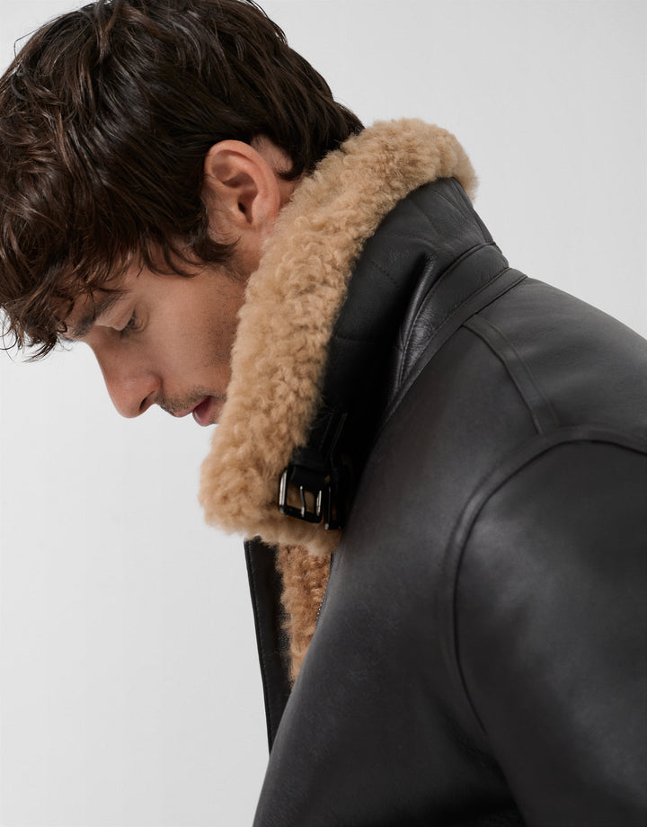 Man wearing a black leather jacket with a fur collar on a light gray background