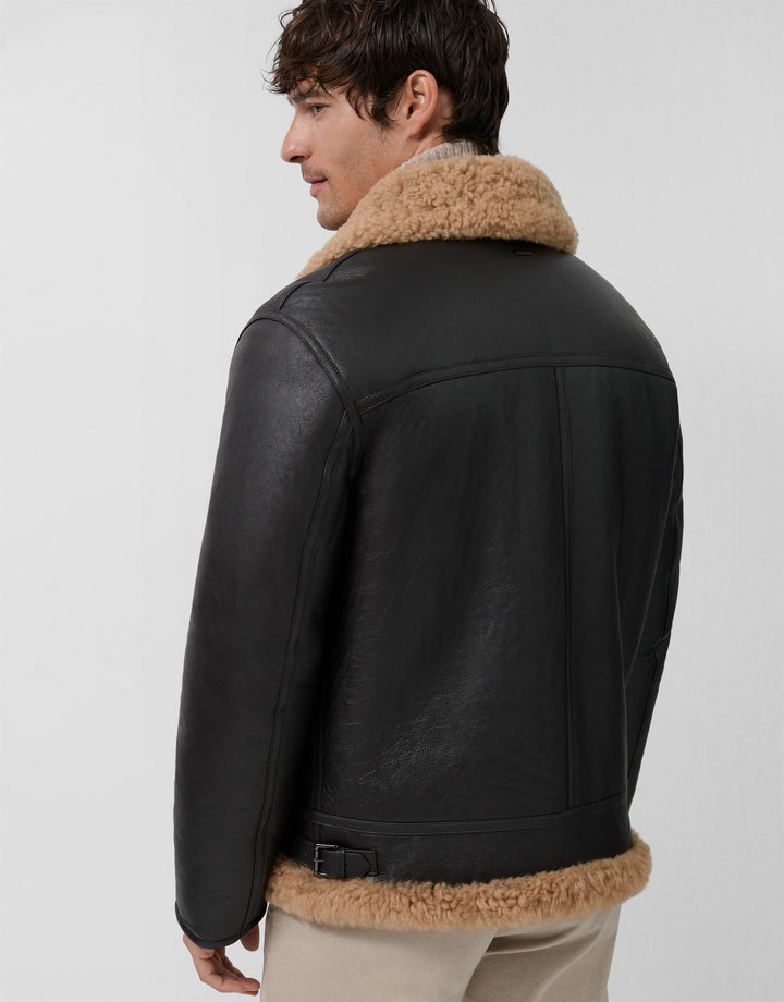 Man wearing a black leather jacket with brown shearling collar and cuffs on a light gray background