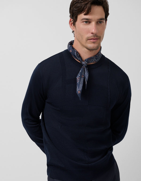 Man wearing a navy sweater with a patterned scarf around his neck against a light gray background