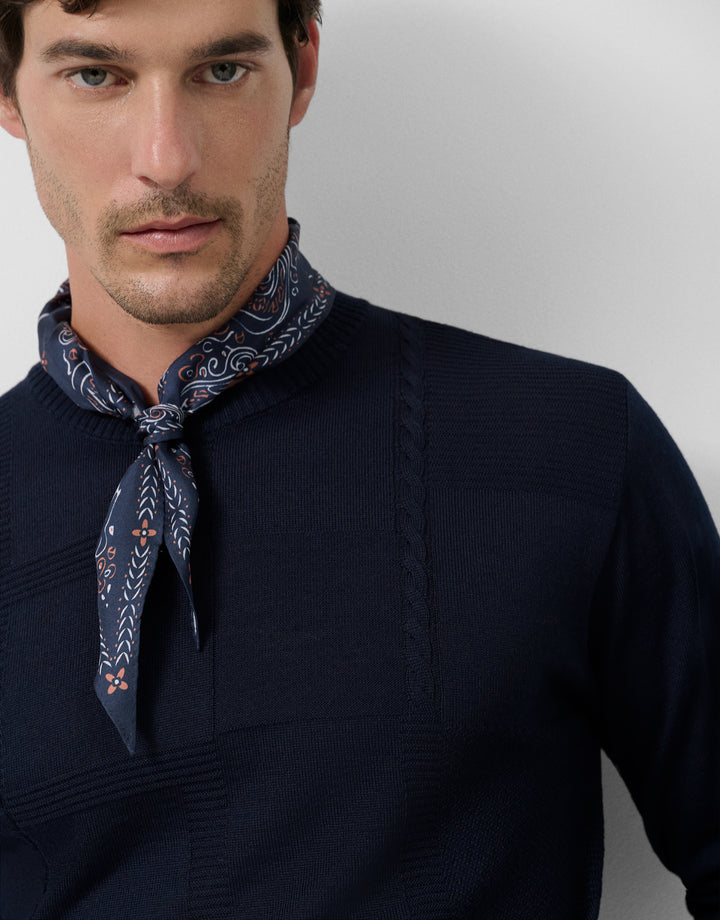 Man wearing a navy sweater and patterned neck scarf against a plain background