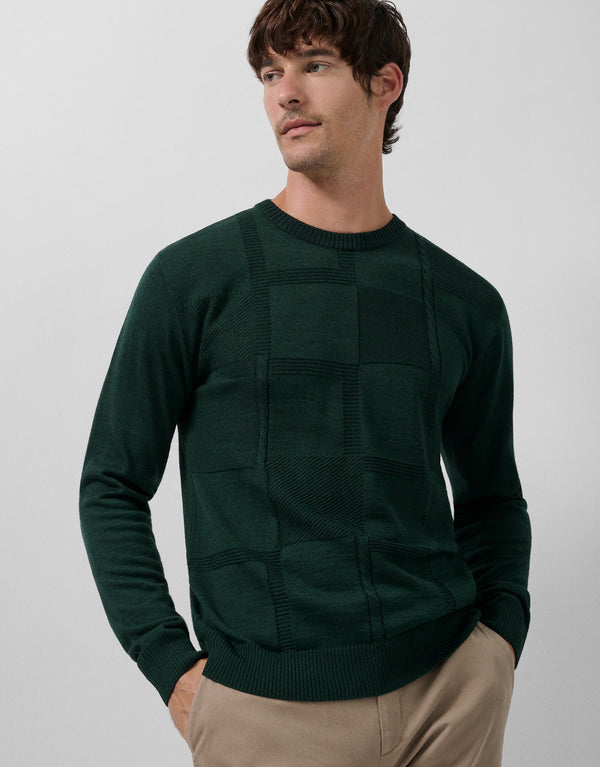 Man wearing a dark green sweater with patchwork design on a plain background