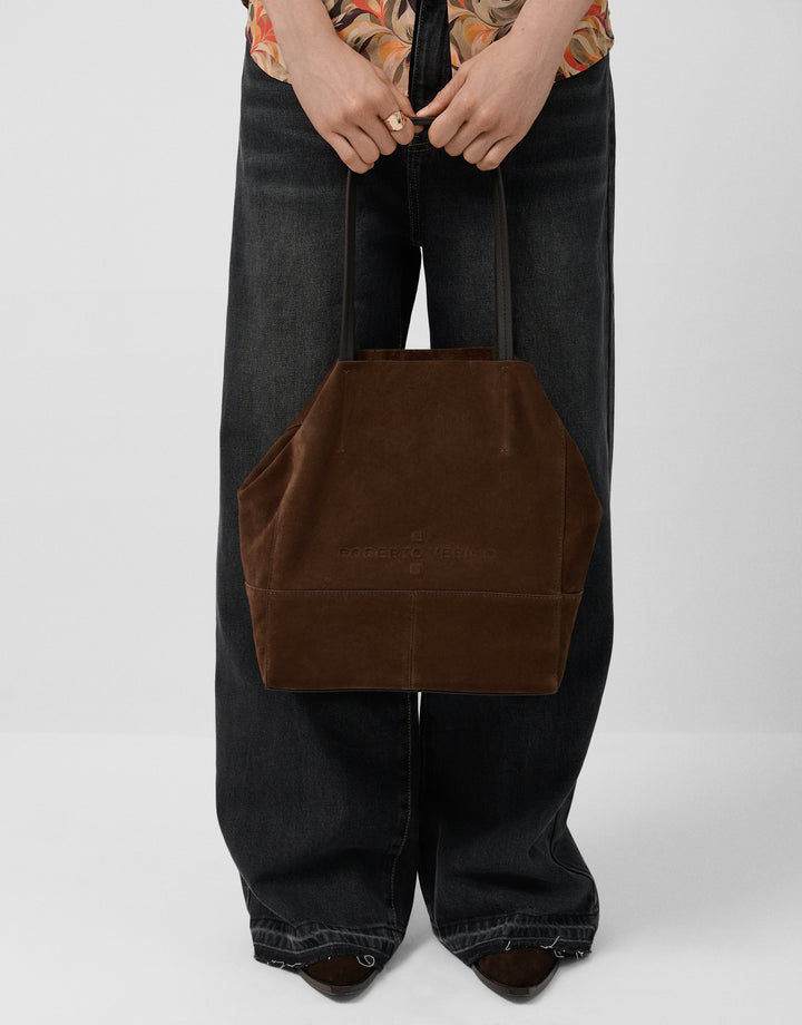 Person holding a brown tote bag against a plain background