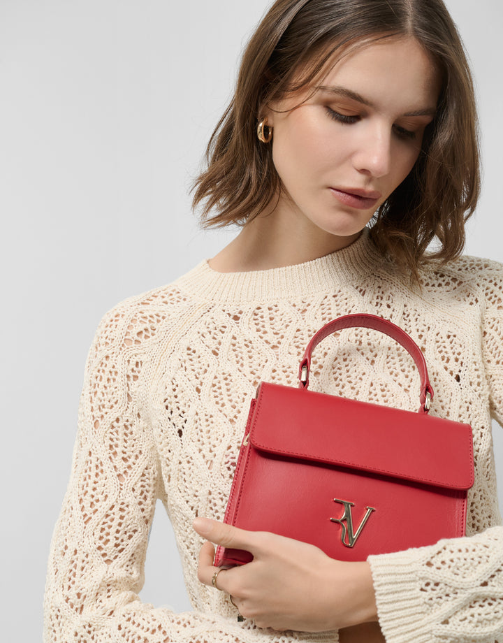 Woman holding a red handbag with a visible brand logo against a light background