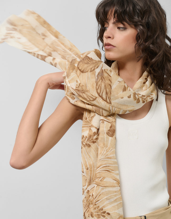 Woman wearing a beige floral scarf against a plain background