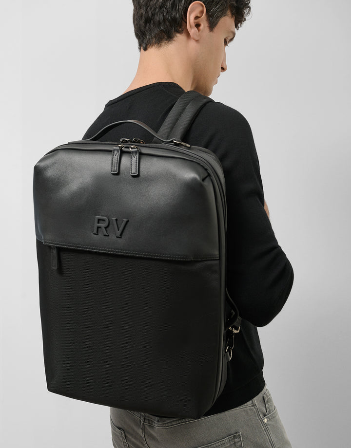 Person wearing a black backpack with 'RV' initials on a plain background