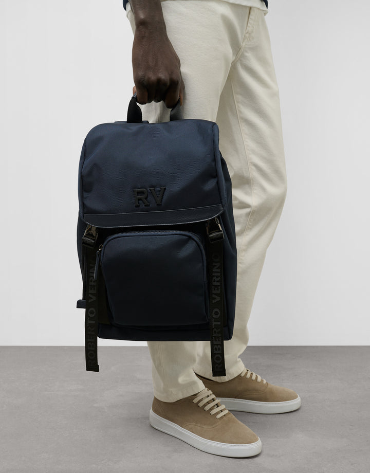 Person holding a navy blue backpack with visible branding on a plain background